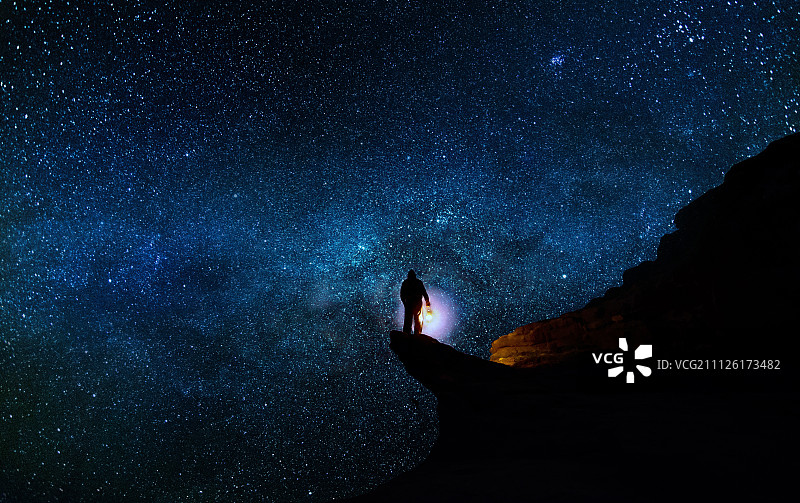 一個人站在懸崖上，身后是星空。圖片素材