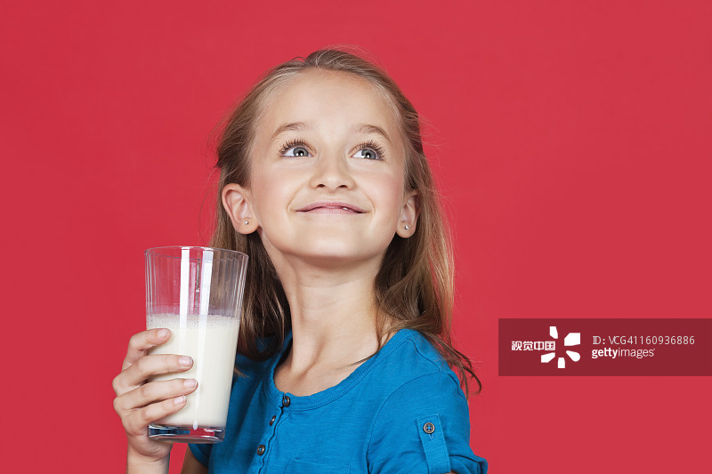 小女孩拿著牛奶杯，抬頭看著紅色的背景圖片素材
