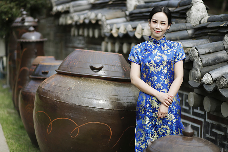 穿著旗袍的女子站在長穴臺，韓國傳統的壇子旁圖片素材