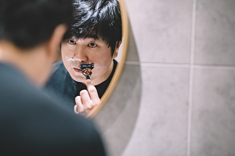 an asian chinese man shaving in the washroom in front of the mirror圖片素材
