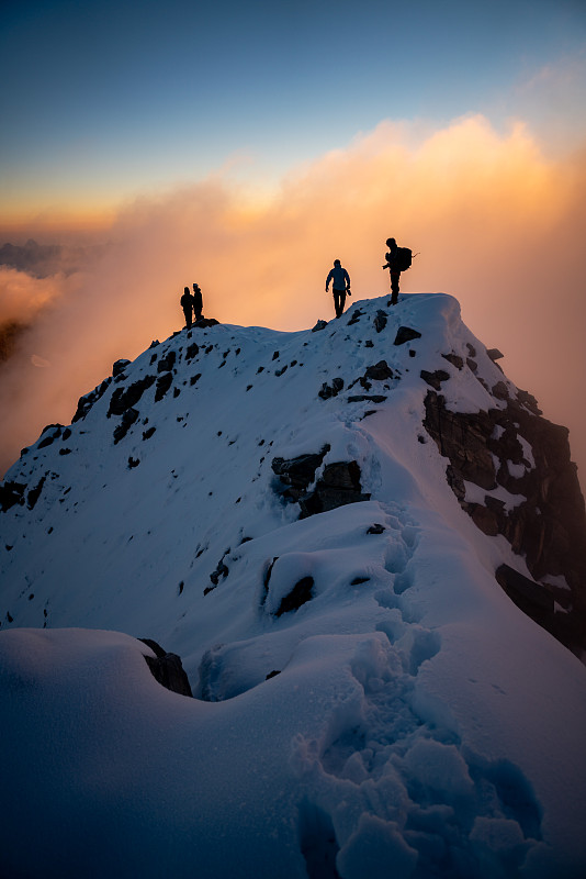 白雪皚皚的山頂上，日出時徒步者的剪影圖片素材