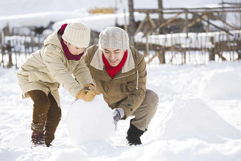快樂的父子倆在雪地上滾雪球圖片素材