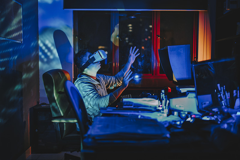 一名亞洲華人男性戴上VR眼鏡，在他的家庭辦公室自修室里，在他的臺式電腦前體驗3D虛擬游戲體驗圖片素材