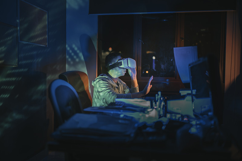 一名亞洲華人男性戴上VR眼鏡，在他的家庭辦公室自修室里，在他的臺式電腦前體驗3D虛擬游戲體驗圖片素材