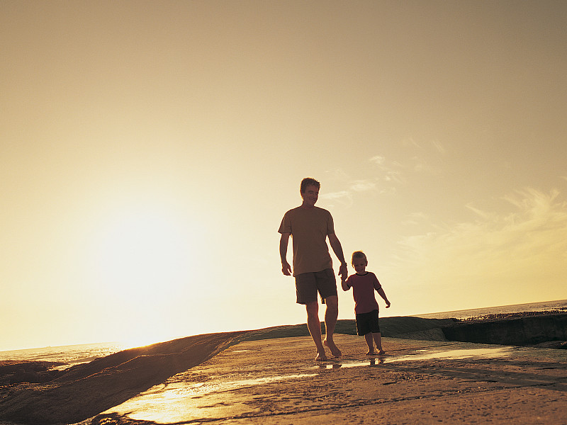 男孩和他的父親在陽光下的海灘上散步圖片素材