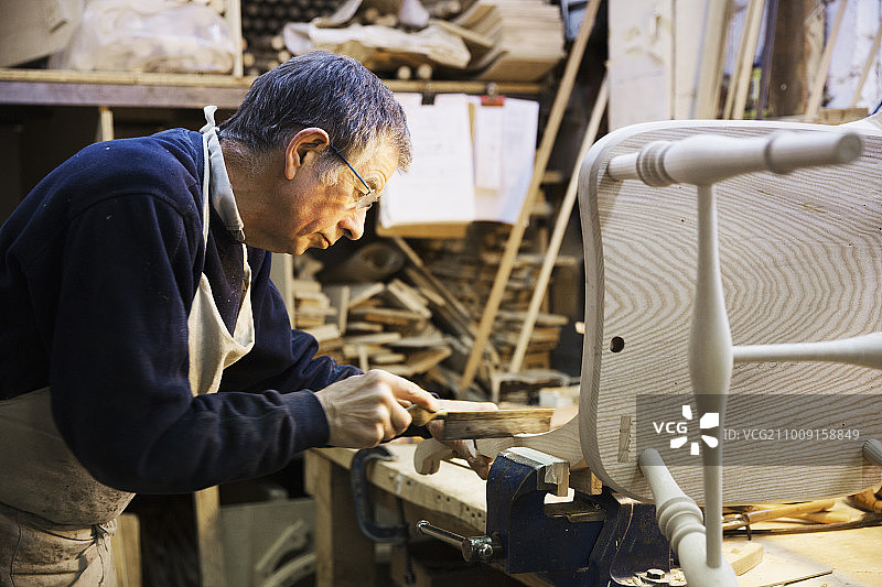 一名男子站在木工车间的工作台上，坐在一把木椅上工作。图片素材