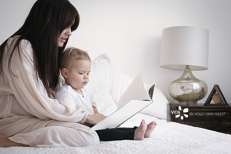 一个大肚子的女人和她的小儿子玩。坐在床上，读故事。图片素材