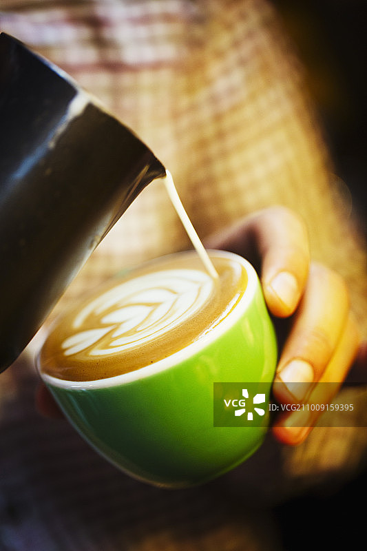 专业咖啡店。一个咖啡师在咖啡的泡沫上创造一个图案。图片素材