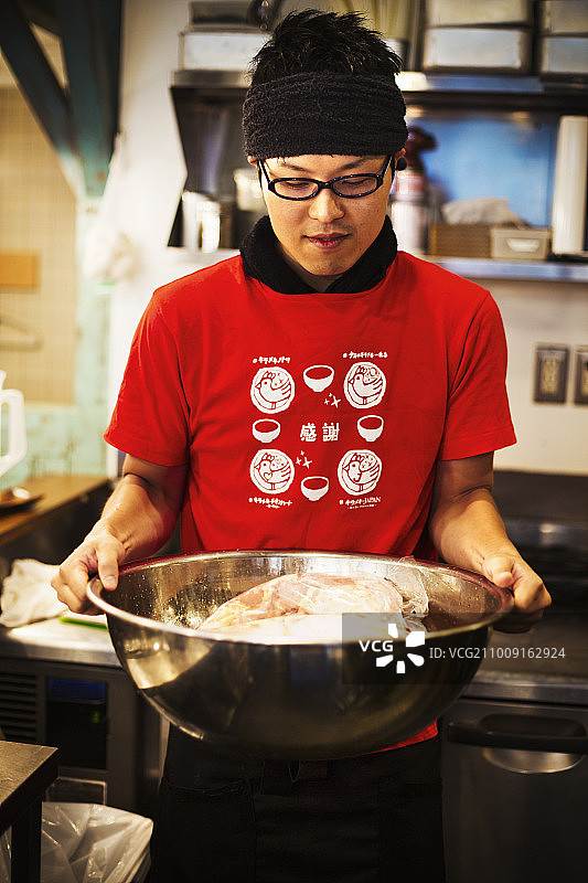 拉面店。一个厨师正在准备一个巨大的金属碗里的肉汤。图片素材