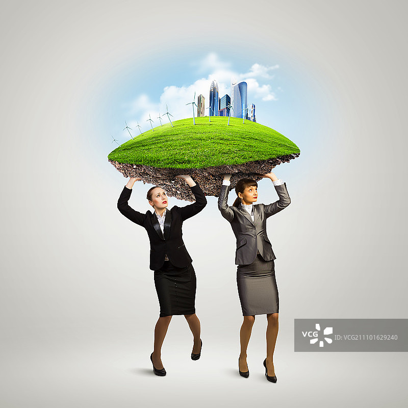 在商业挑战。两个女商人头顶上举着草坪。伙伴关系与生态图片素材