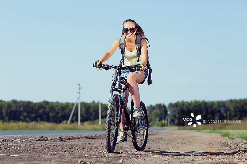 你积极的生活方式。年轻的运动女孩背着背包骑自行车沿着路边图片素材