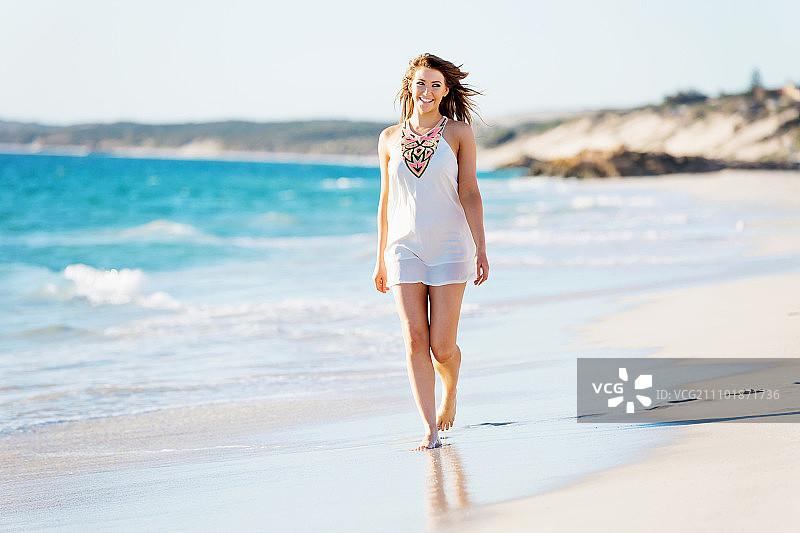 一个年轻女子在海滩上散步。一个年轻漂亮的女人沿着沙滩散步的肖像图片素材
