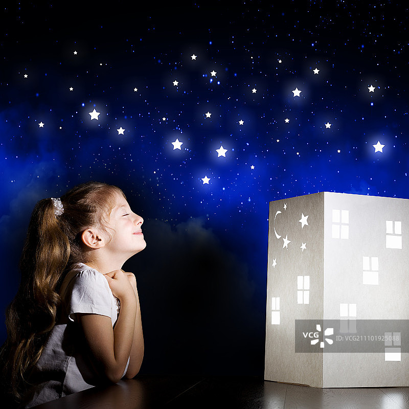 晚上做梦。可爱的小女孩看着房子的模型和梦想图片素材
