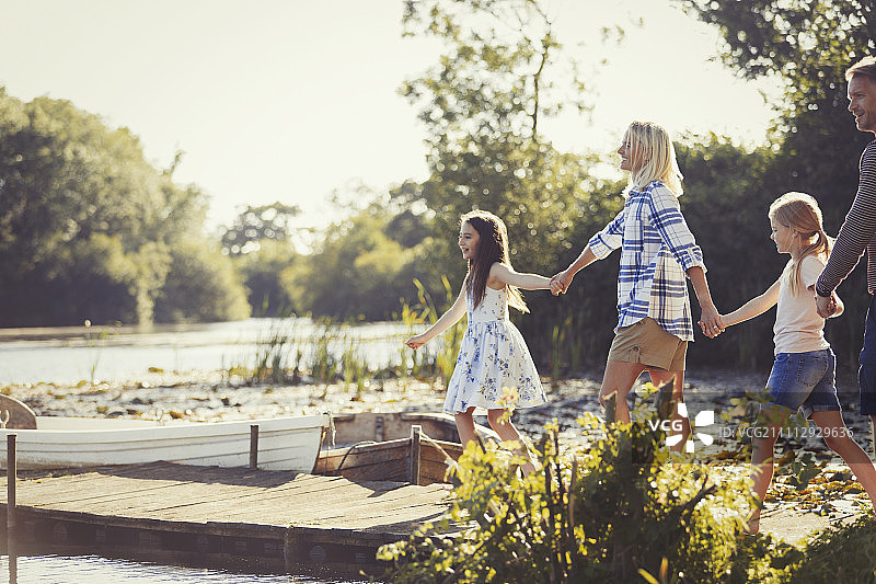 一家人手牵着手走在阳光明媚的湖边码头上图片素材