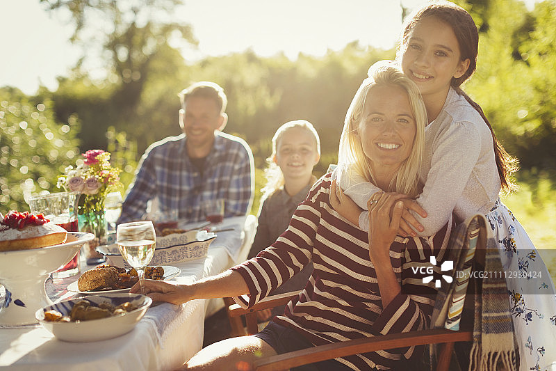 肖像微笑深情的母亲和女儿拥抱在阳光灿烂的花园派对露台桌子图片素材