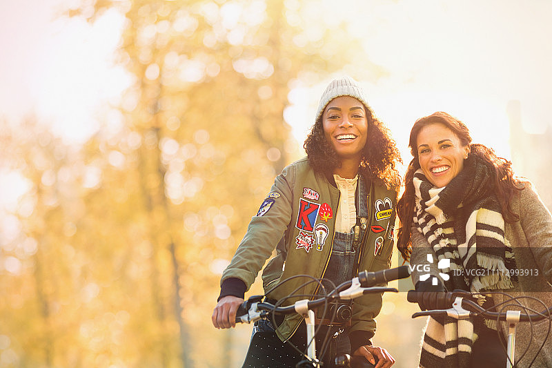 肖像微笑的年轻女性朋友骑在秋天的街道上图片素材