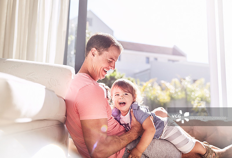 慈爱的父亲抱着婴儿儿子在阳光明媚的客厅图片素材