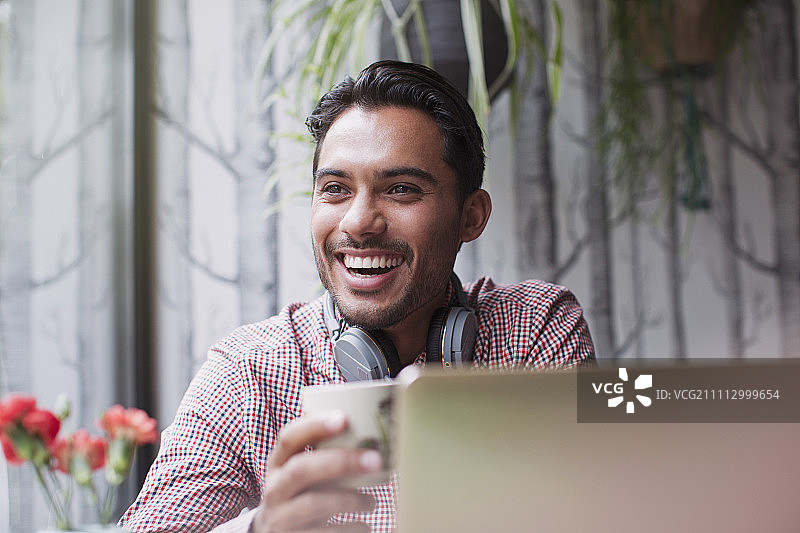 一名男子在咖啡馆边笑边用笔记本电脑喝咖啡图片素材