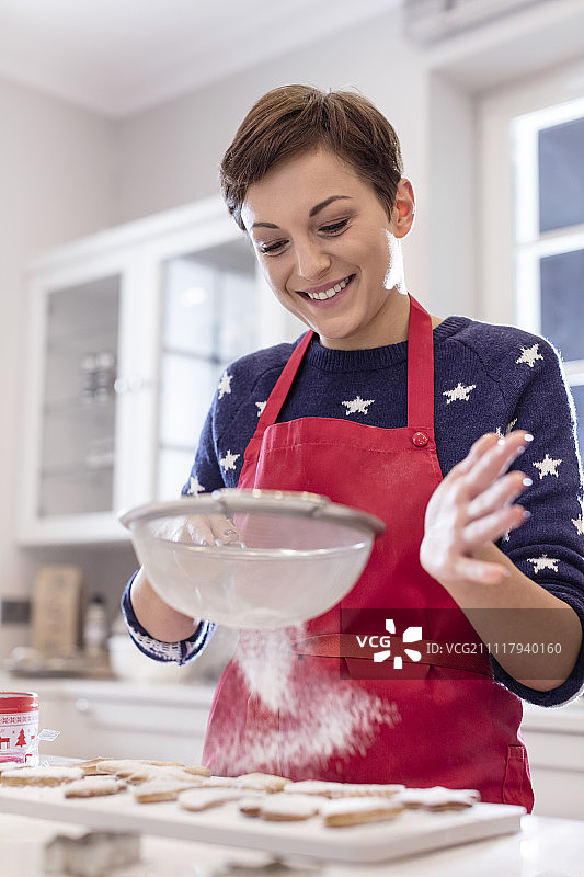 微笑的女人在厨房烘焙，在饼干上筛糖图片素材
