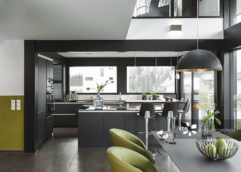 开放式的设计师厨房是灰色的，带有一个烹饪岛和一个用餐区，前面有绿色的软垫椅子图片素材