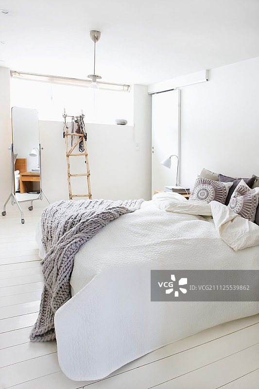 淡灰色的双人床，针织毯，斯堪的纳维亚式卧室，白色木地板;装饰梯子和全长镜在背景图片素材