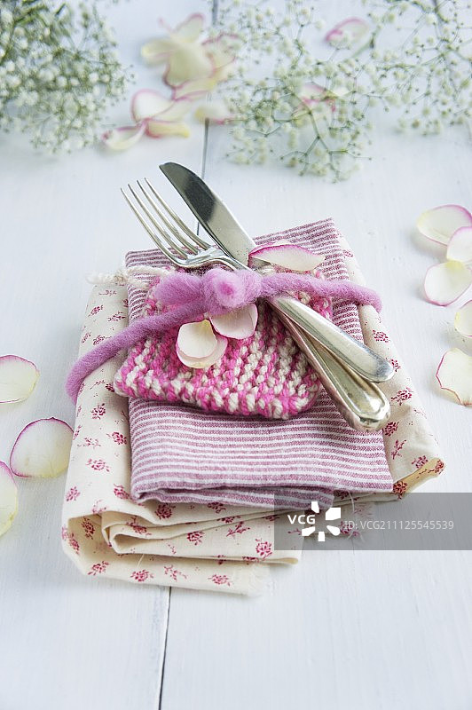 一堆花和条纹织物和餐具用毛毡丝带系上，并撒上花瓣图片素材