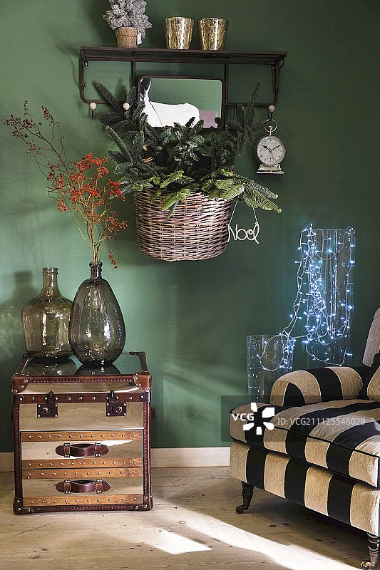 条纹扶手椅，玻璃器皿中的仙女灯，边桌上的大肚酒瓶，绿色墙上的圣诞装饰品篮子图片素材