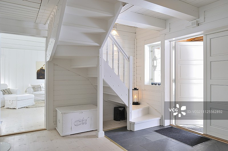 门厅有蜿蜒的木制楼梯，可以看到整个粉刷成白色的客厅和白色的家具图片素材