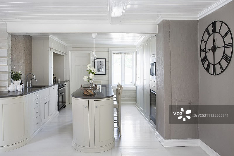 开放式设计的厨房配有独立的柜台，墙上挂着漆成暖灰色的大钟图片素材
