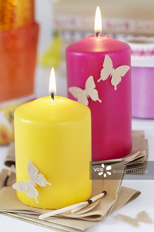 牛皮纸杯垫上放着色彩鲜艳的蜡烛，上面装饰着打孔的纸蝴蝶图片素材