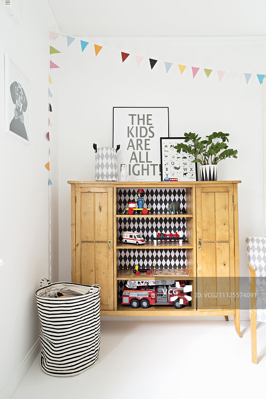 在儿童卧室的角落里，木制餐具柜的开放式书架上摆放着玩具和黑白条纹的篮子，墙上挂着五颜六色的彩旗图片素材
