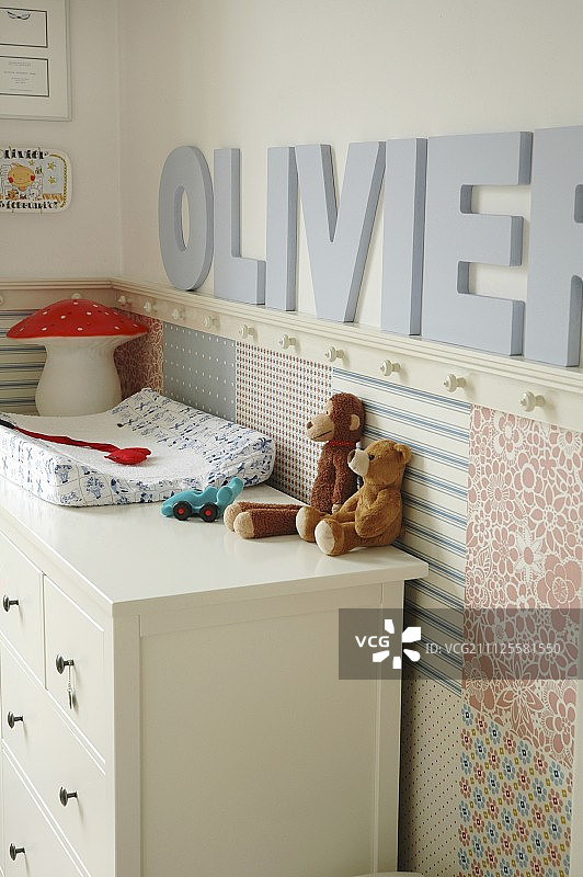 幼儿室角落的白色抽屉柜上放着毛绒玩具，墙上挂着装饰性的字母图片素材