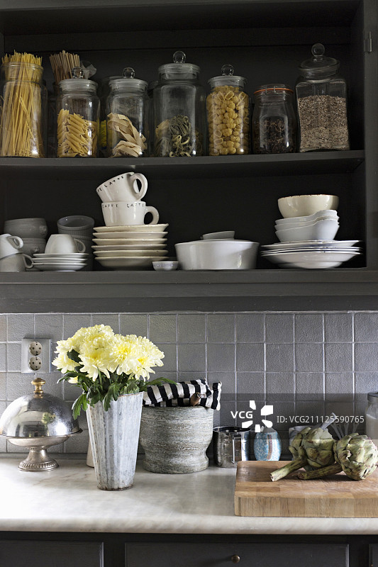 在厨房的柜台上放着花瓶，花瓶的下方是白色的陶罐和开着门的壁柜中的储物瓶图片素材