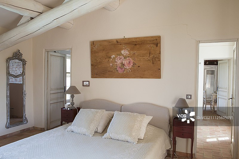 木梁天花板下的双人床上散布着靠垫;打开一扇门，可以看到旁边的房间图片素材