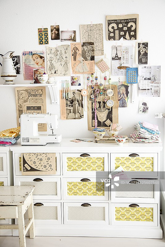 白色抽屉柜上方的墙上装饰着复古时尚杂志的剪报和缝纫机的剪报图片素材
