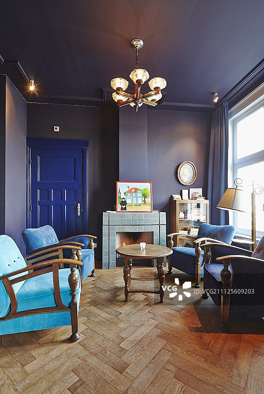 蓝色的沙龙，人字形拼花地板，各种色调的蓝色扶手椅和开放式壁炉的背景图片素材