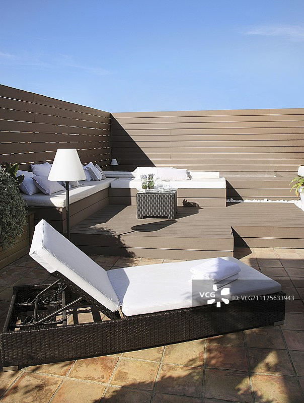 在阳光充足的屋顶露台上，配有靠垫的优雅躺椅和长椅图片素材