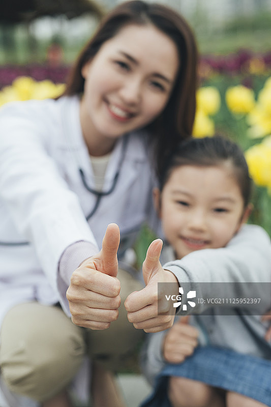 微笑的女医生和小女孩在花园里举着大拇指图片素材