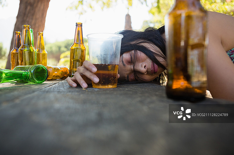 一个醉醺醺的女人在公园里拿着一杯啤酒睡在桌子上图片素材