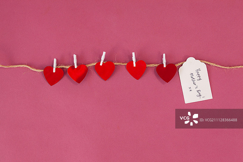 母亲节快乐卡片和红心挂在绳子上，粉红色的背景图片素材