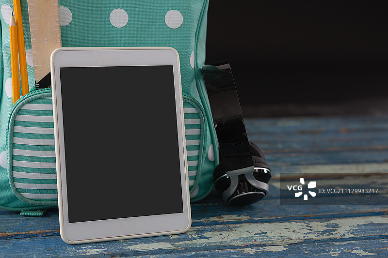 书包、耳机和数码平板电脑放在桌子上，背景是黑色图片素材