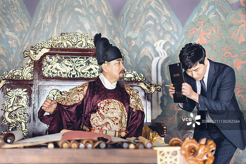 穿着韩国国王服装的高级男子训斥拿着剪贴板的现代年轻商人图片素材