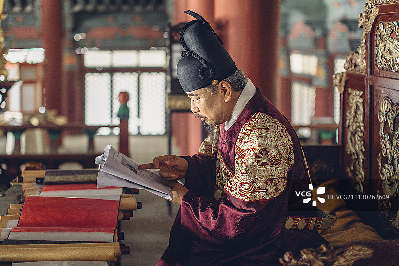 穿韩王服的老人坐在王位上看报纸的侧视图图片素材