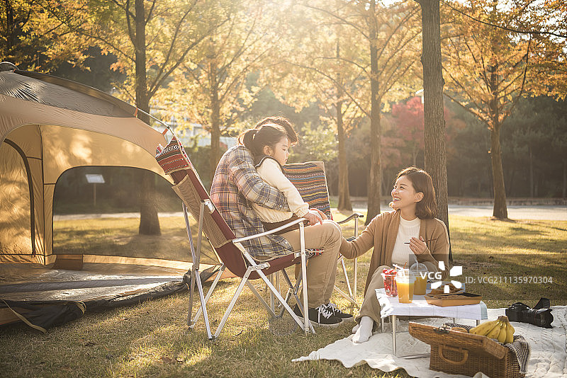 秋天，一家人坐在折叠椅上野餐，母亲在公园里喂女儿图片素材