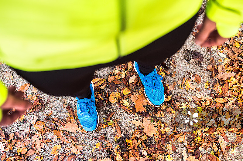 年轻的跑步者站在秋天公园的水泥小路上。图片素材