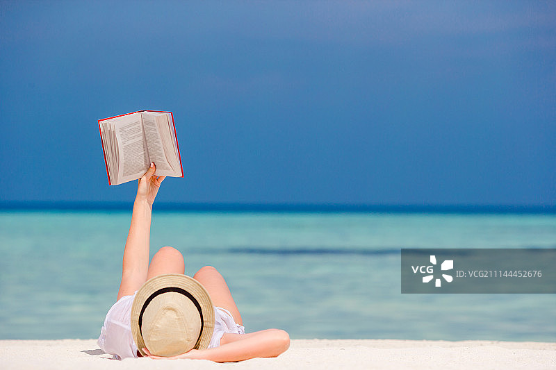 小女孩躺在热带的白色沙滩上看书图片素材
