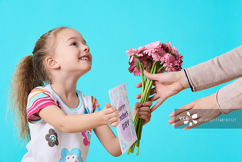 母亲节快乐。可爱的小女孩给妈妈贺卡和一束粉红色的非洲菊…图片素材