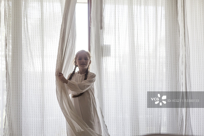 穿着睡衣的女孩站在挂着窗帘的窗户旁图片素材