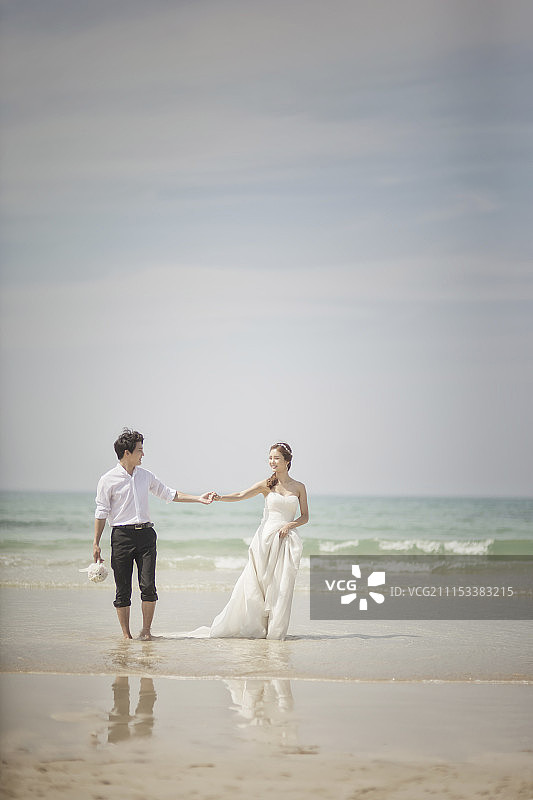新娘和新郎手牵着手在海滩上散步图片素材