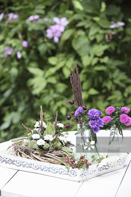 用白色紫苑，蓟和罂粟籽装饰的花环旁边的粉红色紫苑玻璃瓶图片素材